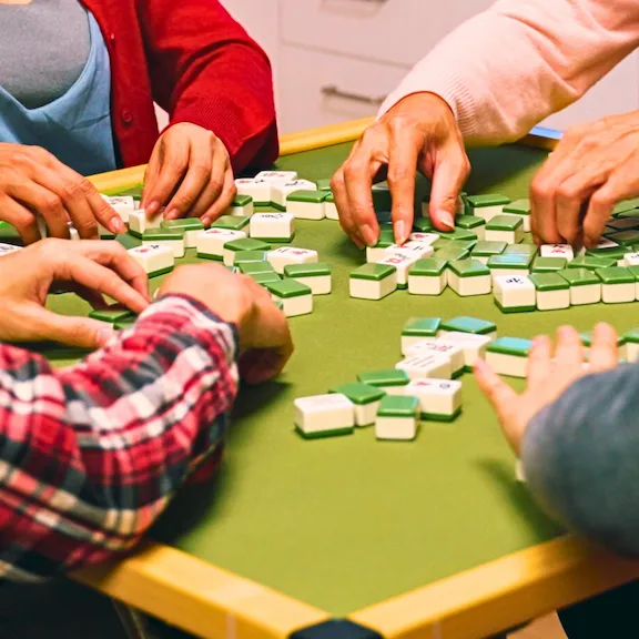 Four people's hands strategically arranging tiles on a Mahjong table